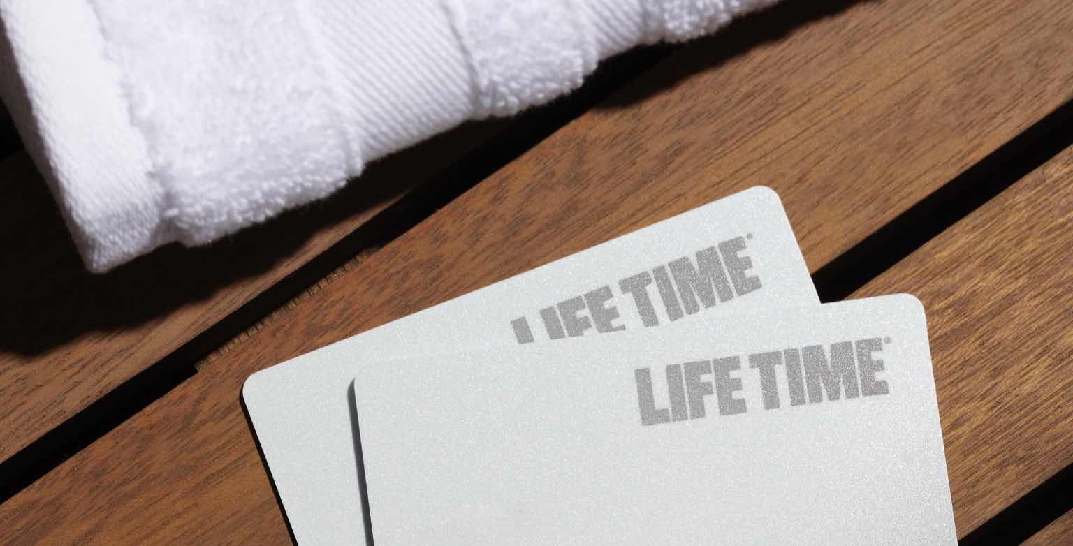 A photo of two Life Time membership cards on a wooden bench.