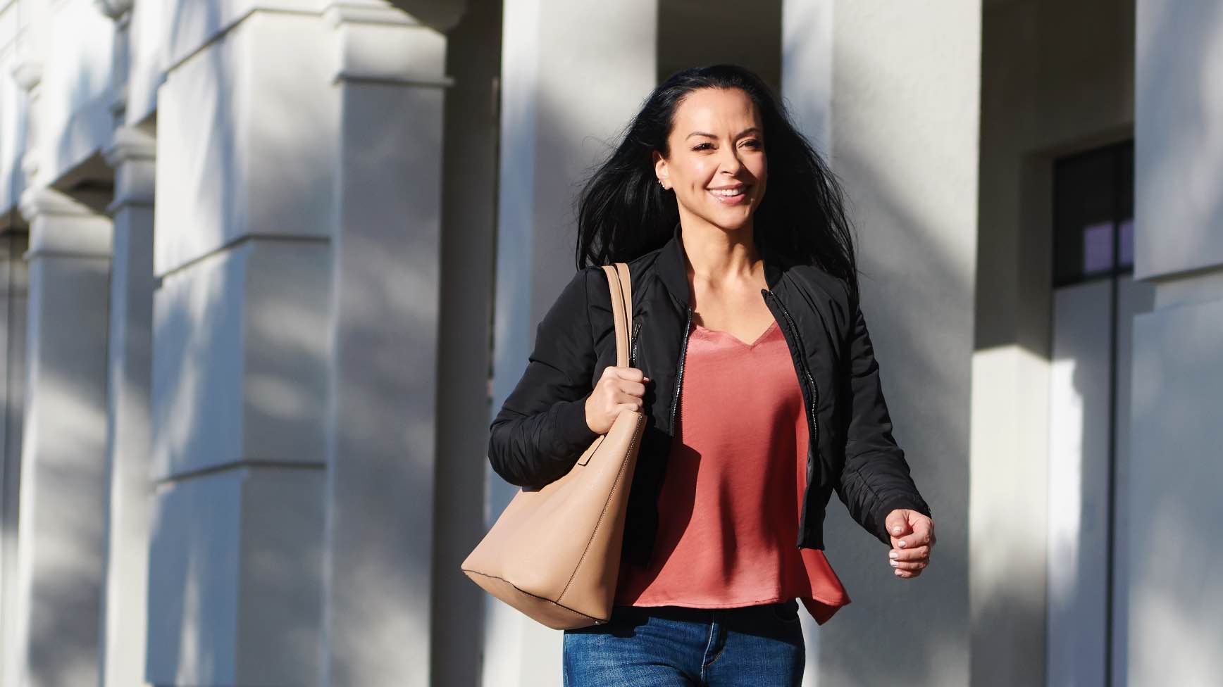 woman walking down sidewalk, holding tote bag