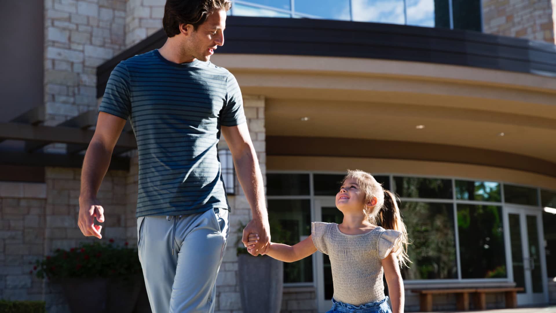 A father and daughter walk together in front of a Life Time Athletic Resort and Spa