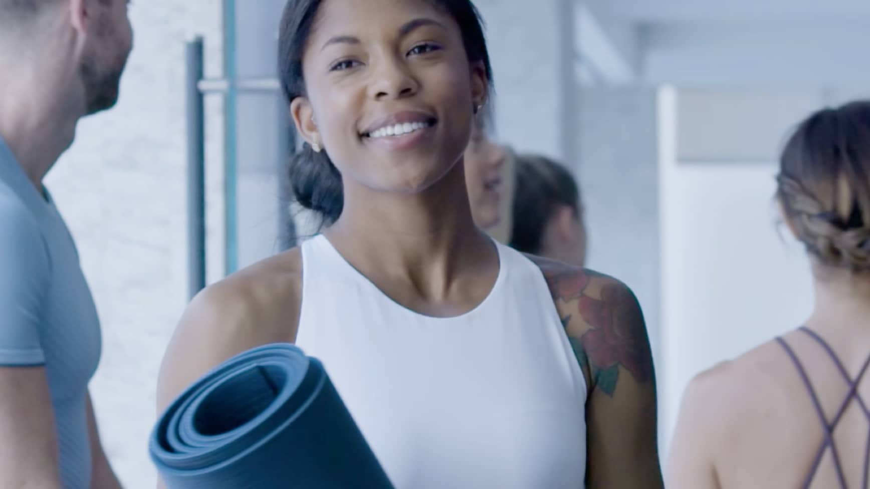 A Life Time Living resident in a white tank top holds a yoga mat and smiles