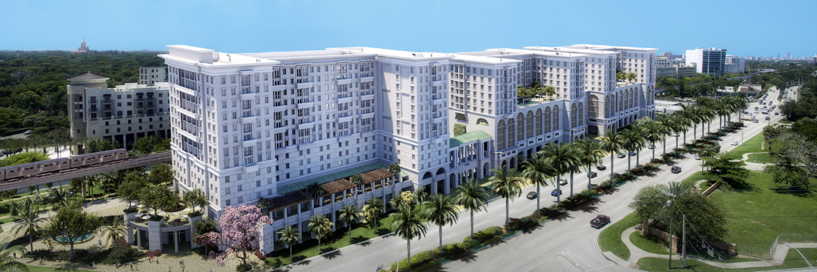 Aerial view of Life Time Coral Gables community, featuring a palm tree-lined boulevard and a light rail train passing the Life Time residences, coworking space and athletic club.