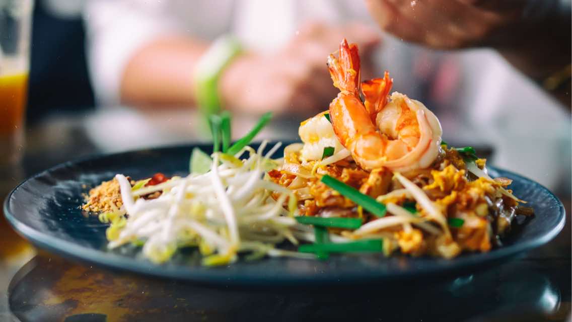 Shrimp pad thai elegantly presented on a navy dinner plate