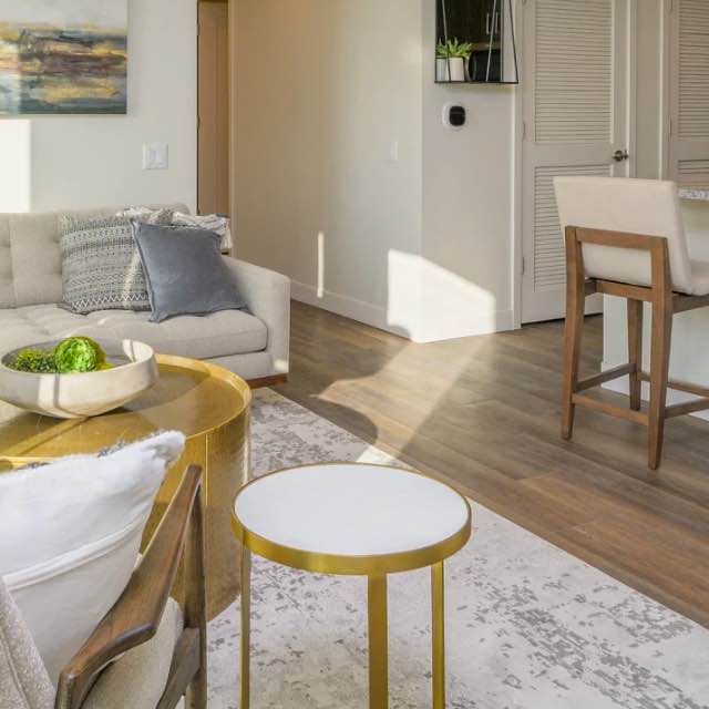 picture of living room with white sofa, wooden coffee table and chair, looking at the kitchen counter with two wooden counter chairs and white closet doors
