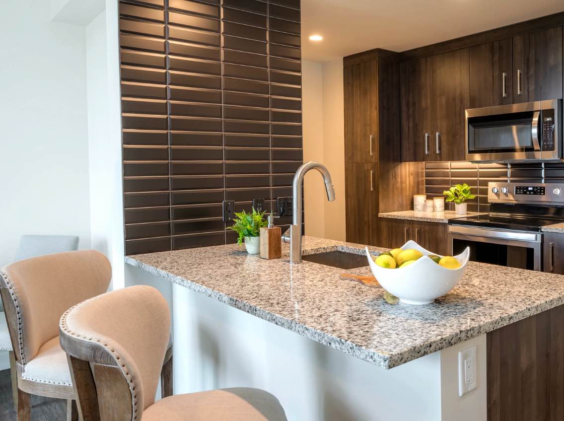 photo of kitchen with dark brown cabinets, granite counter top, stainless steel appliances and counter stools